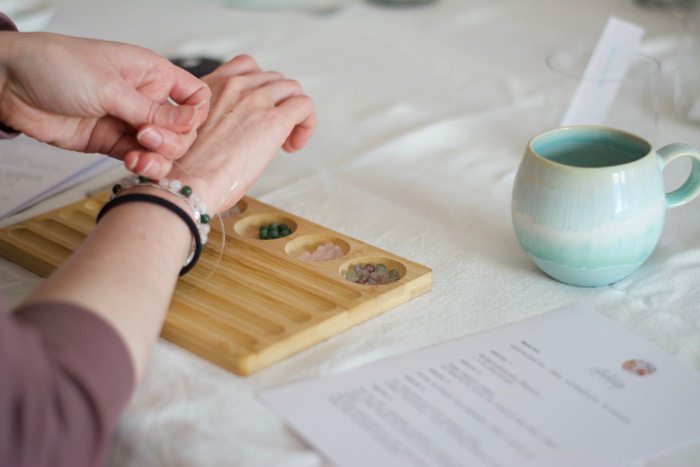 Teilnehmerin fädelt ihr Armband, daneben Perlen und eine Tasse Tee